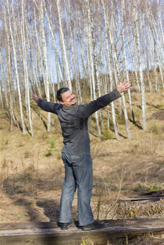 Man stands arms outstretched as if embracing the birch grove, stock photo