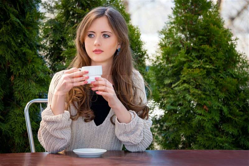 Beautiful young woman drinking hot coffee or tea in the morning at restaurant. Lifestyle photo, girl enjoying her morning coffee in summer garden, stock photo