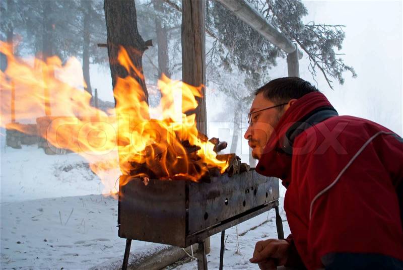 Man fanning the fire in the grill on winter forest, stock photo