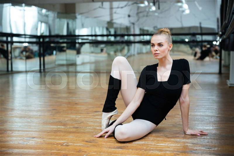 Young charming ballerina sitting on the floor and looking away in ballet class, stock photo
