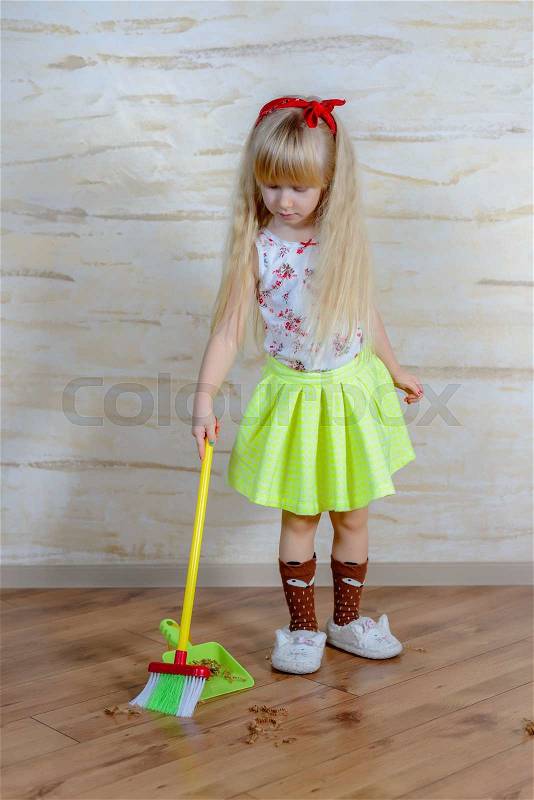 Pretty little blond girl cleaning the house with a colorful plastic toy broom and pan bending forward as she carefully sweeps up the dirt, full length close up, stock photo