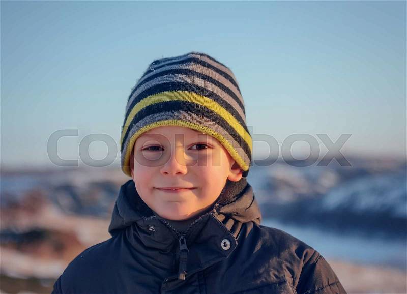 Portrait Happy little boy in winter clothing having fun in fresh white winter snow in evening light, stock photo
