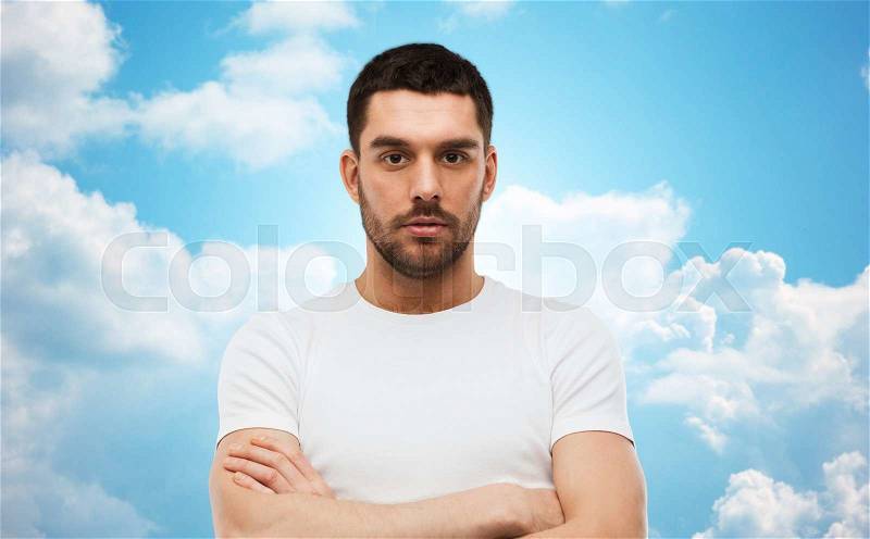 People concept - young man with crossed arms over blue sky and clouds background, stock photo