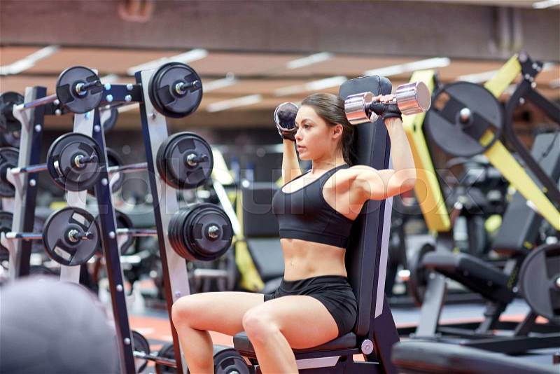Sport, fitness, bodybuilding, weightlifting and people concept - young woman with dumbbell flexing muscles in gym from back, stock photo