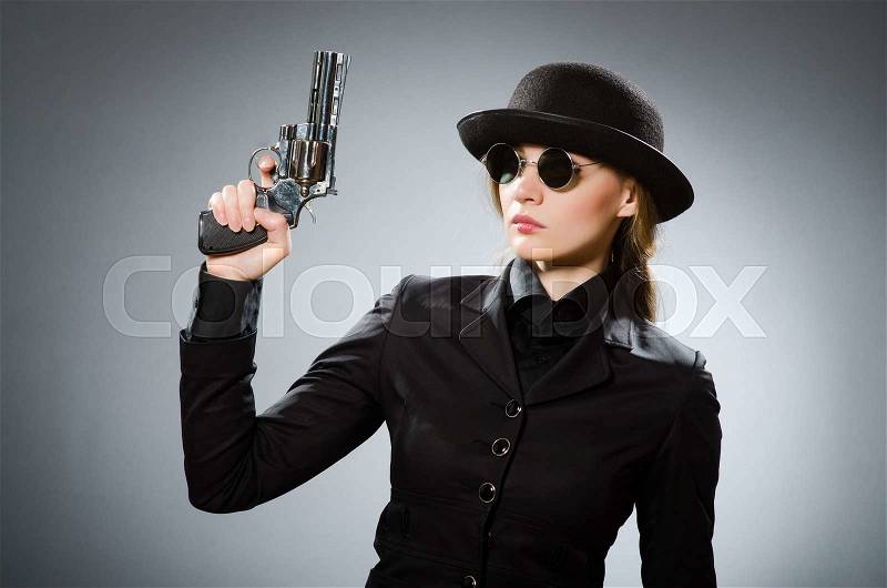 Female spy with weapon against gray, stock photo