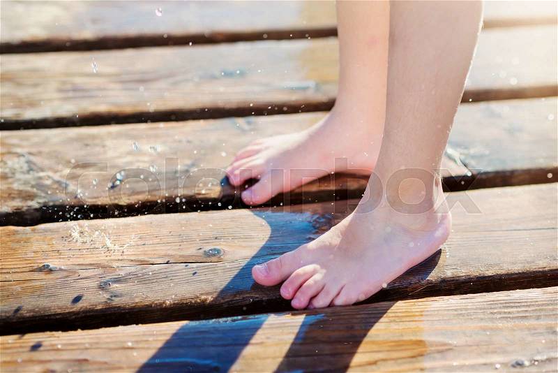 Close up of childs wet feet on wooden pier on sunny summer day, stock photo