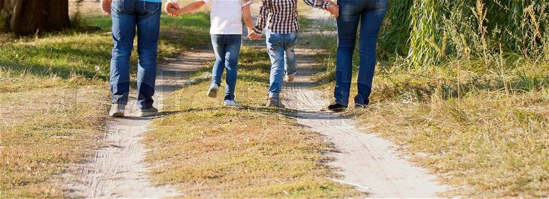 Father, mother, son and daughter walking along the path. Family feet and legs in jeans. Rear view, stock photo