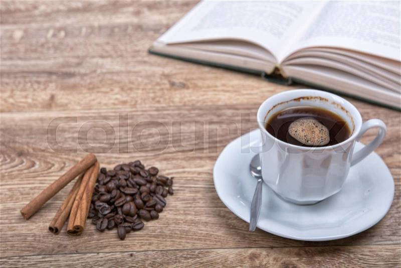 A cup of coffee and cinnamon with a book on a wooden background, stock photo