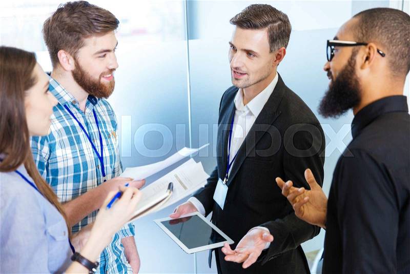 Multiethnic group of young business people standing and talking with chief executive in office, stock photo