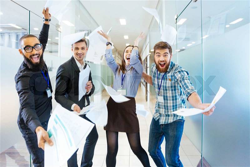 Group of joyful excited business people throwing papers and having fun in office, stock photo