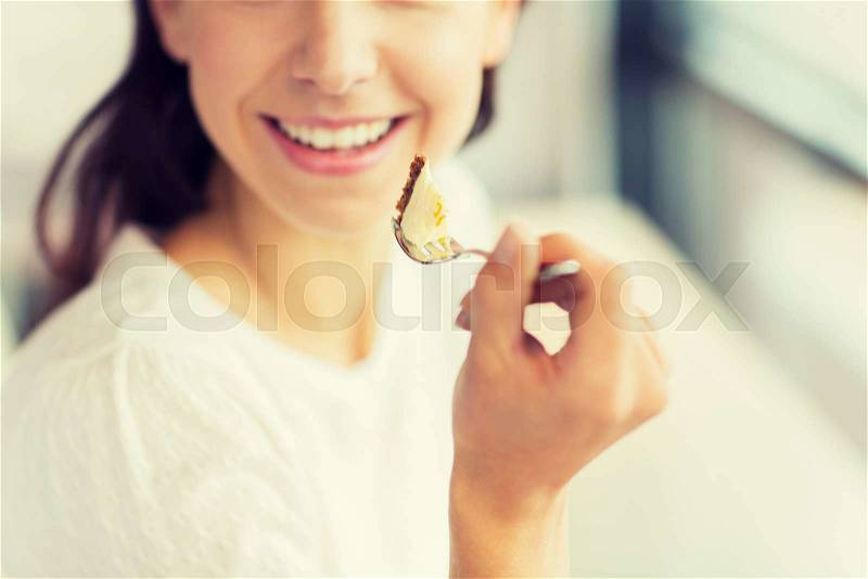 Food, dessert, people and lifestyle concept - close up of smiling young woman holding fork and eating cake at cafe or home, stock photo