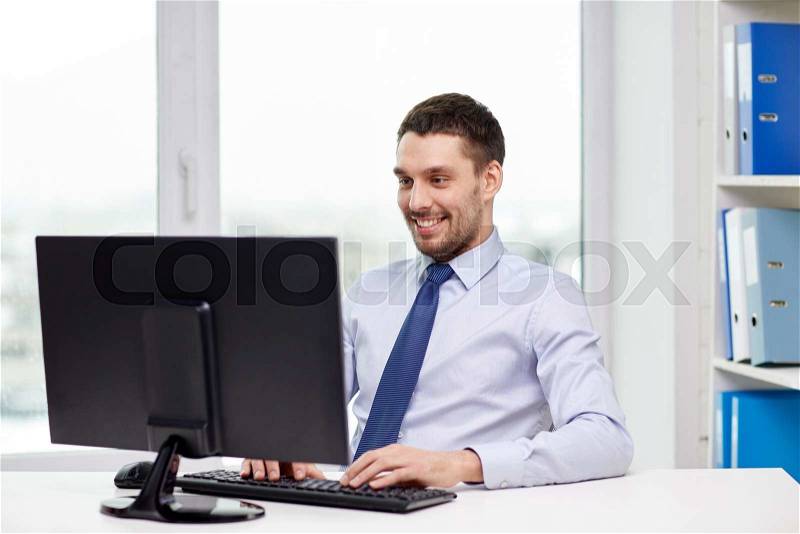 Business, people and technology concept - happy young businessman with computer at office, stock photo