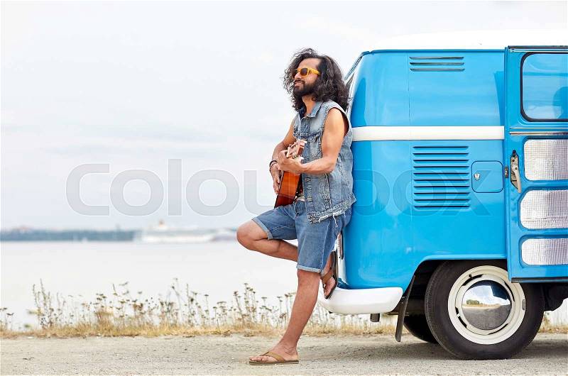 Nature, summer, youth culture, music and people concept - young hippie man playing guitar and singing over minivan car on beach, stock photo