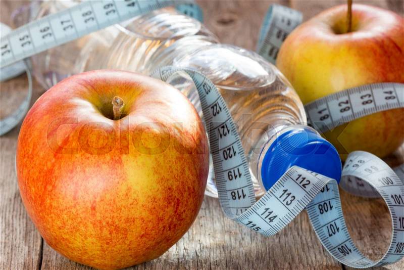 Bottle of water, measuring tape and fresh apples on the wooden background, stock photo