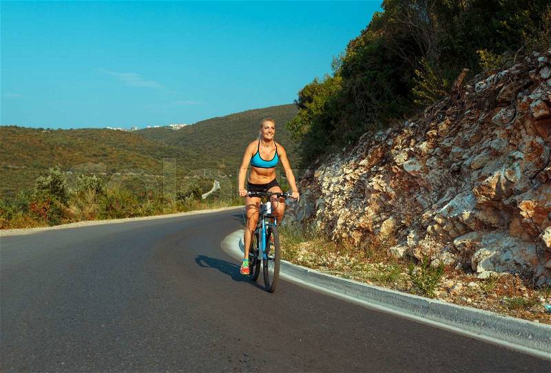 Happy woman cyclist riding a bike on a mountain road, stock photo