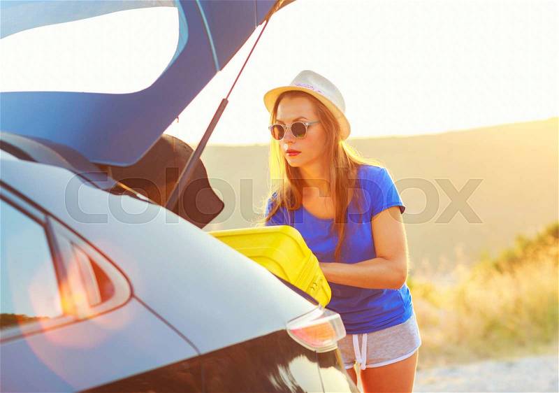 Young woman loading luggage into the back of car parked alongside the road, stock photo