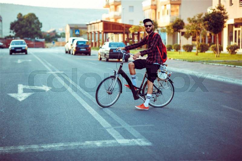 Young stylish man in sunglasses riding a bike on city street, stock photo