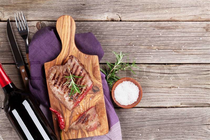 Grilled beef steak with rosemary, salt and pepper and red wine on wooden table. Top view with copy space, stock photo