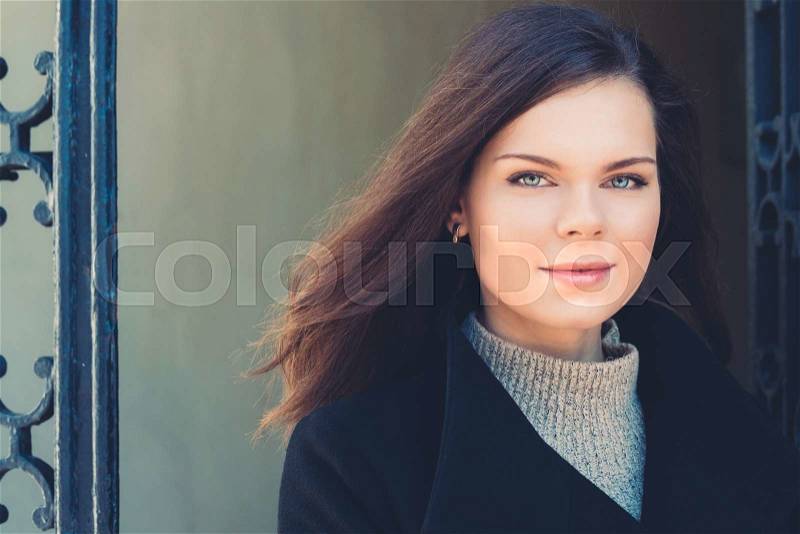 Portrait of a young woman with beautiful eyes in the city. Girl in coat and sweater on a green background, stock photo