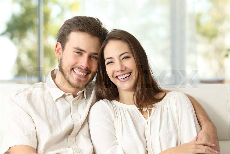 Happy couple sitting on a couch at home and looking at camera, stock photo
