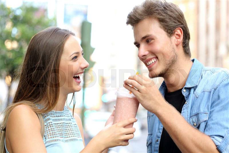 Couple or friends sharing a milkshake and laughing in the street, stock photo