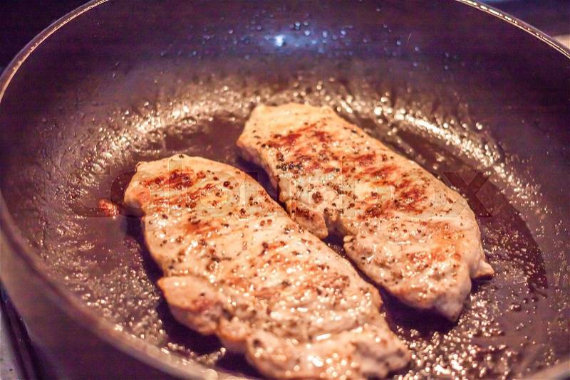 Cooking pork steaks in a frying pan, stock photo