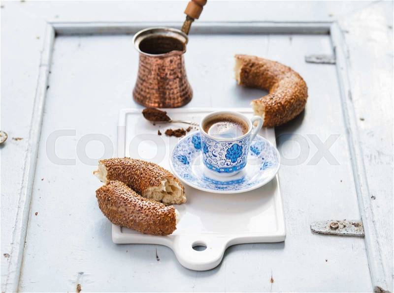 Turkish black coffee served in traditional ceramic cup with pattern, sesame bagel called simit on white serving board over light blue wooden background, selective focus, stock photo
