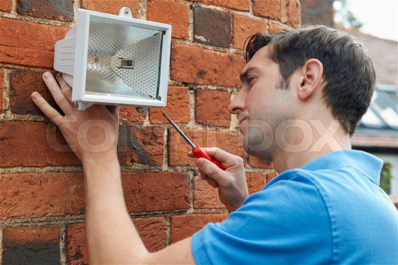 Man Fitting Security Light To Wall Of House, stock photo