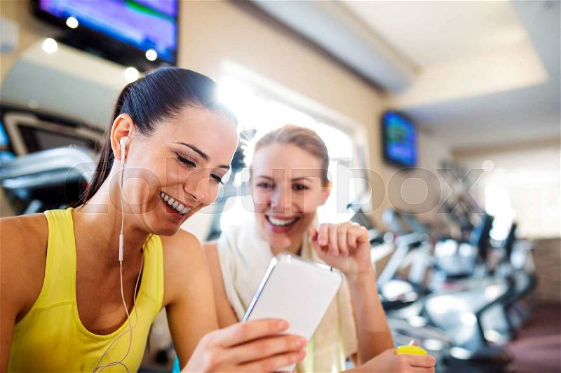 Two attractive fit women in a gym during a break with smart phone, stock photo