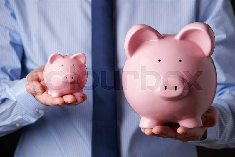 Businessman Holding Large And Small Piggy Bank, stock photo