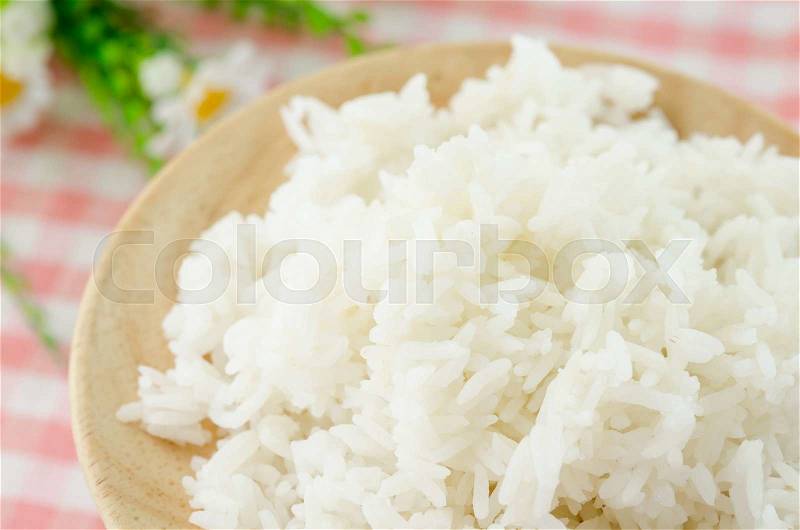 Cooked white rice in wooden dish on tablecloth with flower, stock photo
