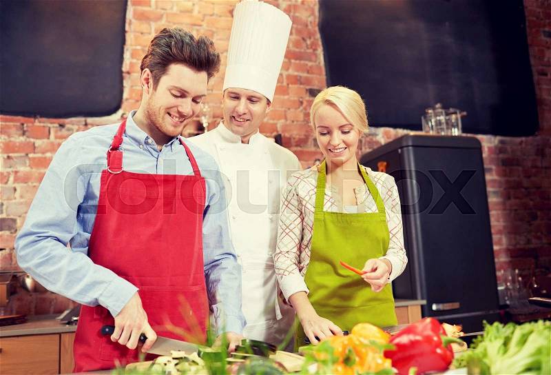 Cooking class, culinary, food and people concept - happy couple and male chef cook cooking in kitchen, stock photo