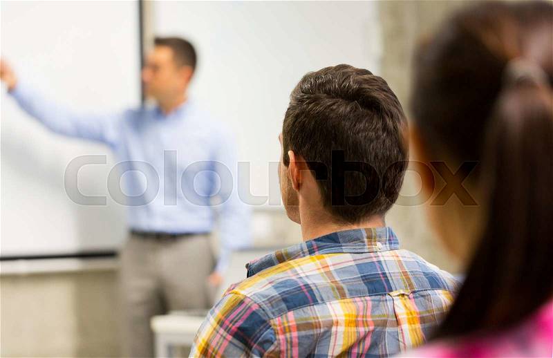 Education, high school, teamwork and people concept - teacher standing in front of students and showing something on white board in classroom, stock photo