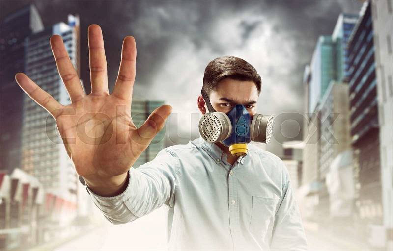 Young man in gas-mask in night town with atmospheric pollution shows stop hand sign, stock photo