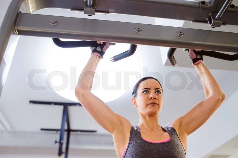 Close up of attractive fit woman in gym doing arms exercises on a machine, stock photo