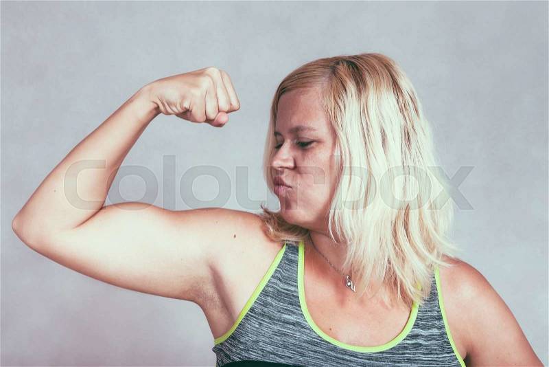 Strong confident muscular woman flexing her muscles. Young blond sporty female showing arm and biceps, stock photo
