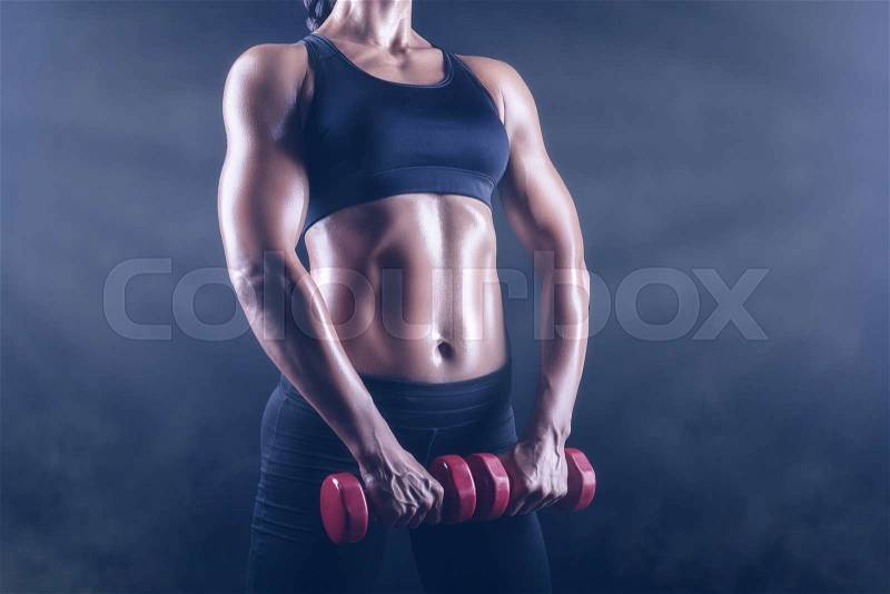 Close up of body fitness girl with dumbbells on a dark background, stock photo