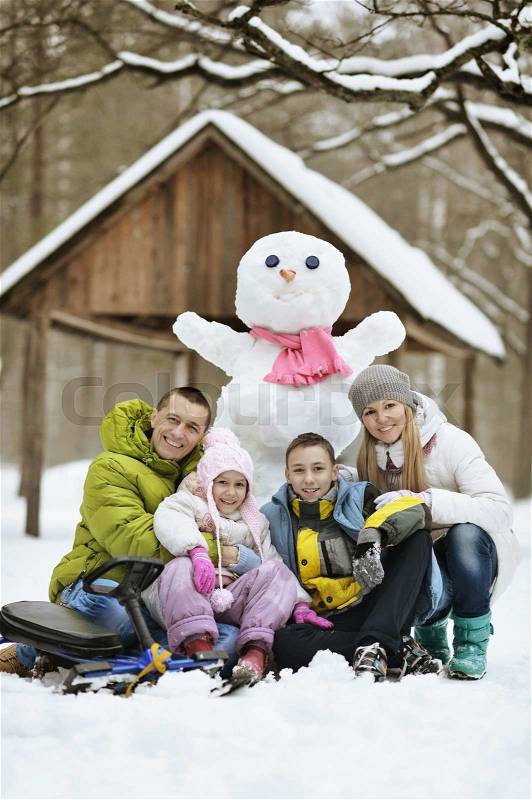 Happy family playing in fresh snow and snowman at beautiful sunny winter day outdoor in nature, stock photo
