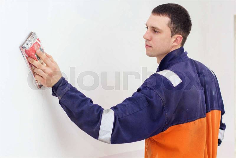 Handyman is doing repair works with sandpaper on a white wall, stock photo