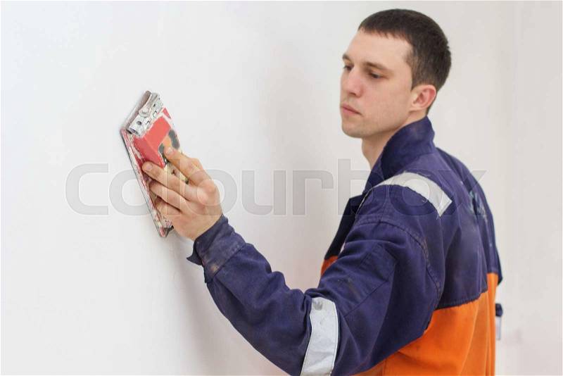 Handyman is doing repair works with sandpaper on a white wall, stock photo