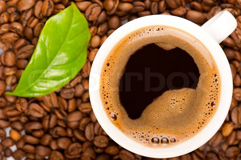 Cup of coffee and coffee beans with green leaf of coffee plant. Focus on cup, stock photo