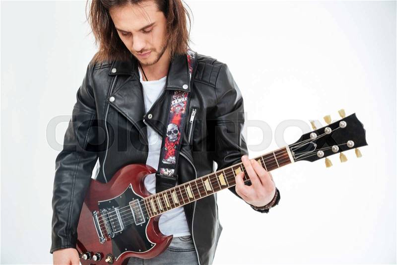Handsome young man with long hair in black leather jacket playing electric guitar over white background, stock photo