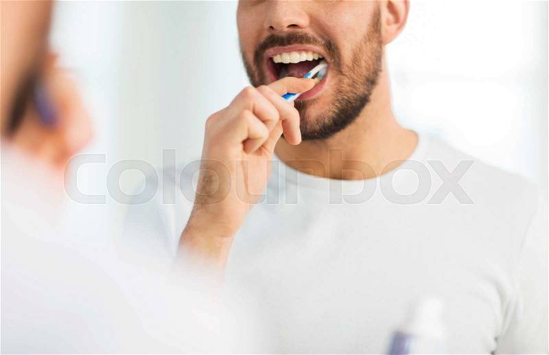 Health care, dental hygiene, people and beauty concept - close up of young man with toothbrush cleaning teeth and looking to mirror at home bathroom, stock photo