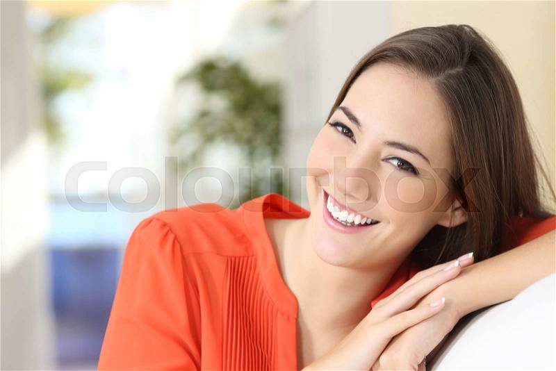Beauty woman with perfect white teeth and smile wearing an orange blouse looking at camera sitting on a couch at home, stock photo