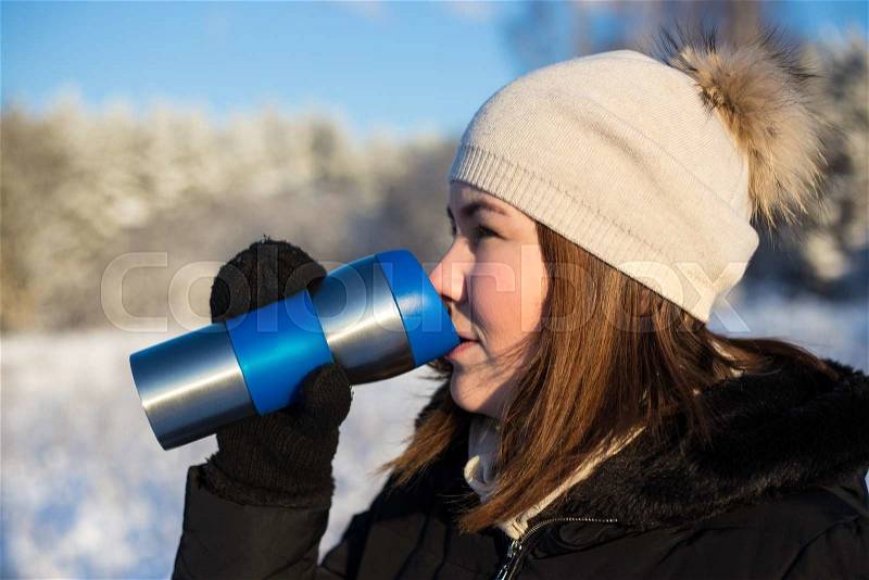 Young beautiful woman with thermal mug in winter forest, stock photo
