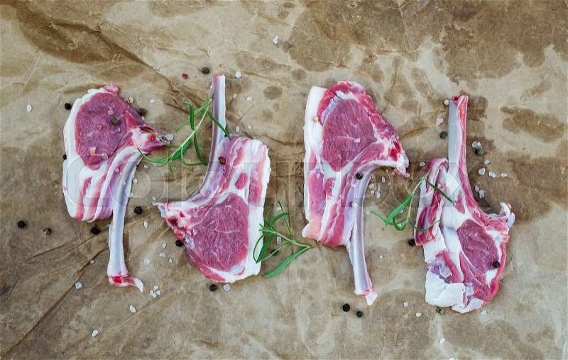 Raw lamb chops. Rack of Lamb with rosemary and spices over oily craft paper background, top view, stock photo