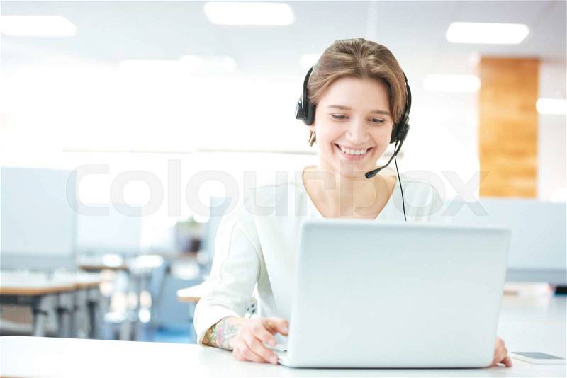 Happy young woman sitting and working with laptop using headset, stock photo