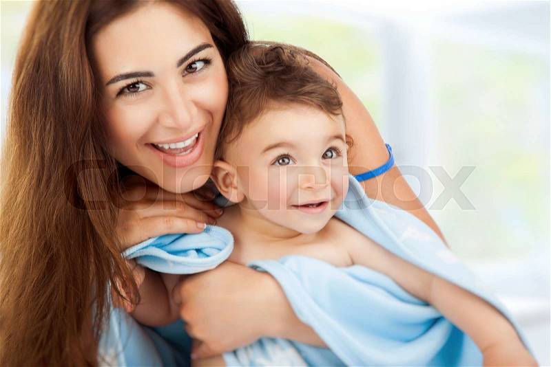 Closeup portrait of beautiful cheerful mother holding on hands cute little son after bath wrapped in towel, child\'s hygiene, happy healthy lifestyle, stock photo