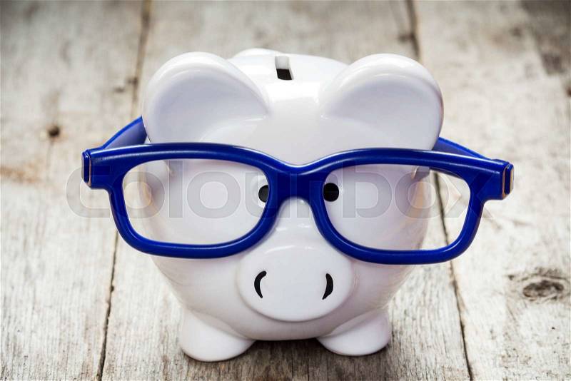 Piggy bank with blue glasses on old wooden floor , stock photo