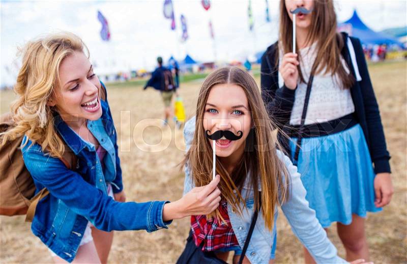 Teenage girls at summer music festival having fun with fake mustache, stock photo